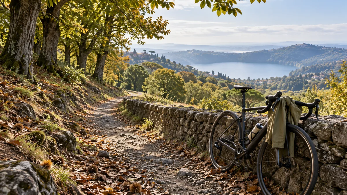 Sentiero tra i castagneti dei Castelli Romani con una bicicletta da strada e una giacca antivento appoggiate a un muretto, lago sullo sfondo